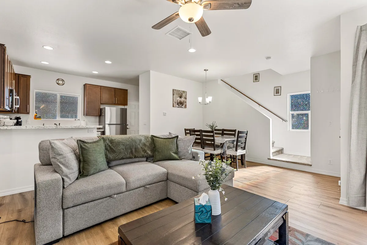 This image captures a spacious open-plan living room with a comfortable sofa, coffee table, dining table, and staircase in view. The arrangement is clearly designed for both relaxing and entertaining, offering ample space for gatherings or cozy movie nights.
