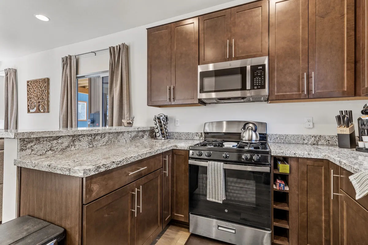 A welcoming kitchen featuring a granite countertop, stainless steel appliances, and warm wooden cabinets. Kitchen utensils are displayed, creating an inviting atmosphere for group cooking or family gatherings.
