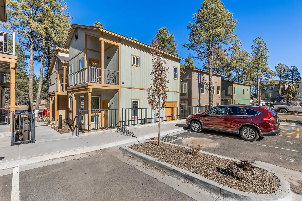 A two-story building with visible balconies set amidst tall trees, hinting at the private spaces attached to the residence. The exterior shot includes the parking area and showcases how the balconies nestle into the wooded setting, illustrating the home’s integration with mountain scenery and Ponderosa Pines.