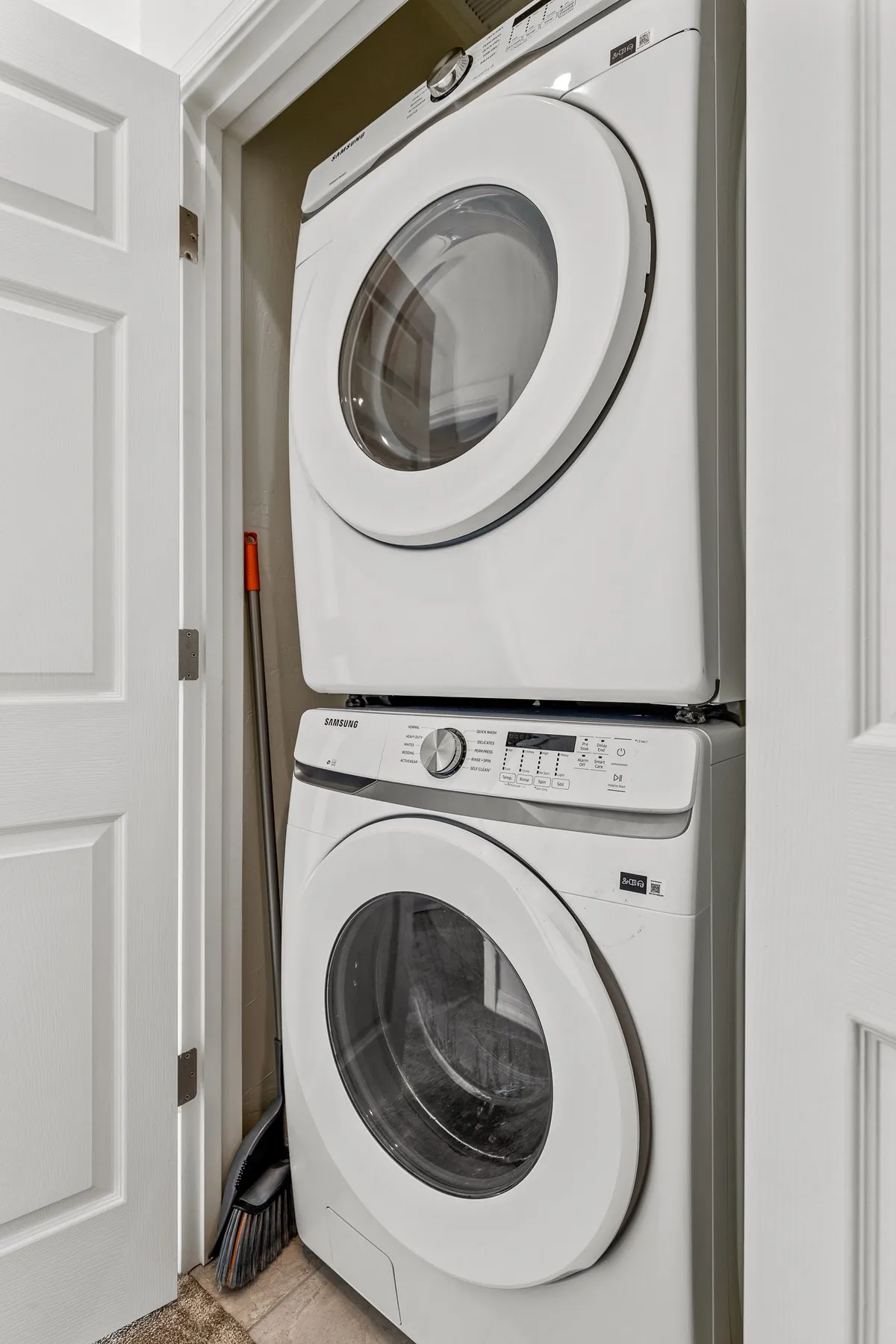 A practical laundry area with a stacked washer and dryer, neatly organized cleaning supplies, and a glimpse of the home's tidy interior. This space ensures guests can easily refresh clothes during longer stays.