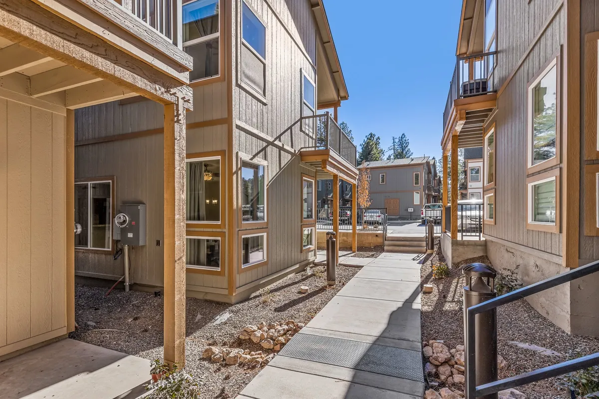 This exterior shot features a landscaped pathway leading past building facades with charming balconies and vibrant greenery. The scene feels inviting and hints at a walkable, community-oriented environment, echoing downtown Flagstaff’s lively setting.