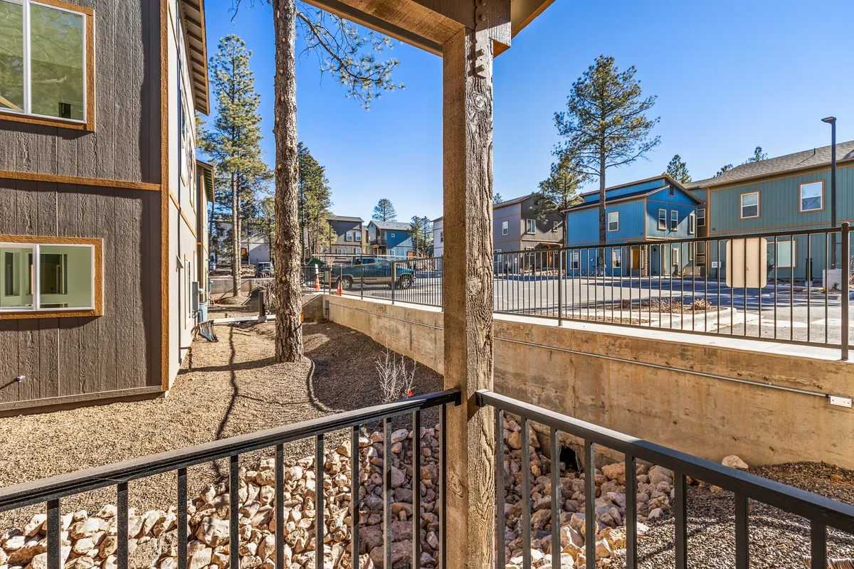 An exterior view from a balcony, featuring a wooden railing and an expansive backdrop of mature trees. The vantage point provides a feeling of elevation and privacy, ideal for quiet moments or intimate gatherings, while also visually connecting the balcony to its natural surroundings.