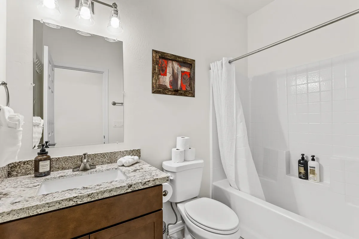 A bright, inviting bathroom with a granite countertop, large mirror, white towels, and tasteful artwork. The clean, spa-like setting suggests a place for relaxation and self-care after a busy day.