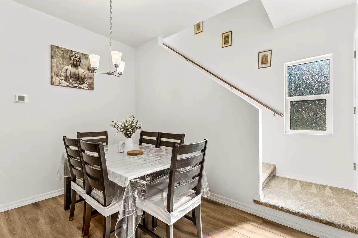 This image shows a warmly lit dining area with a distinct chandelier, a central dining table, and large windows that offer a glimpse toward the outside. The scene is set for family meals or friendly gatherings, with a feeling of anticipation and connectivity.